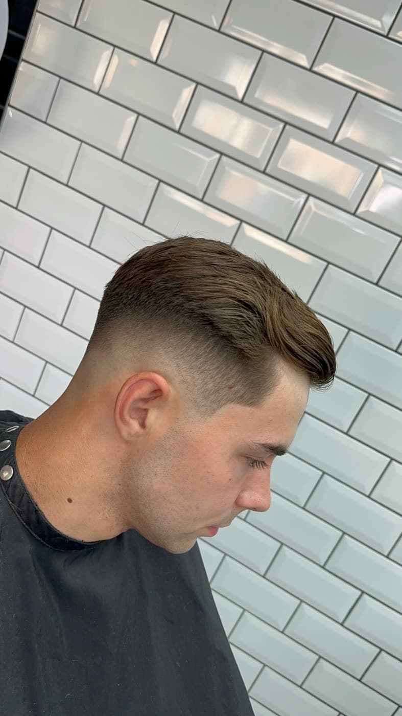 Side-swept textured crop with a clean low skin fade, against the shop's white subway tiles