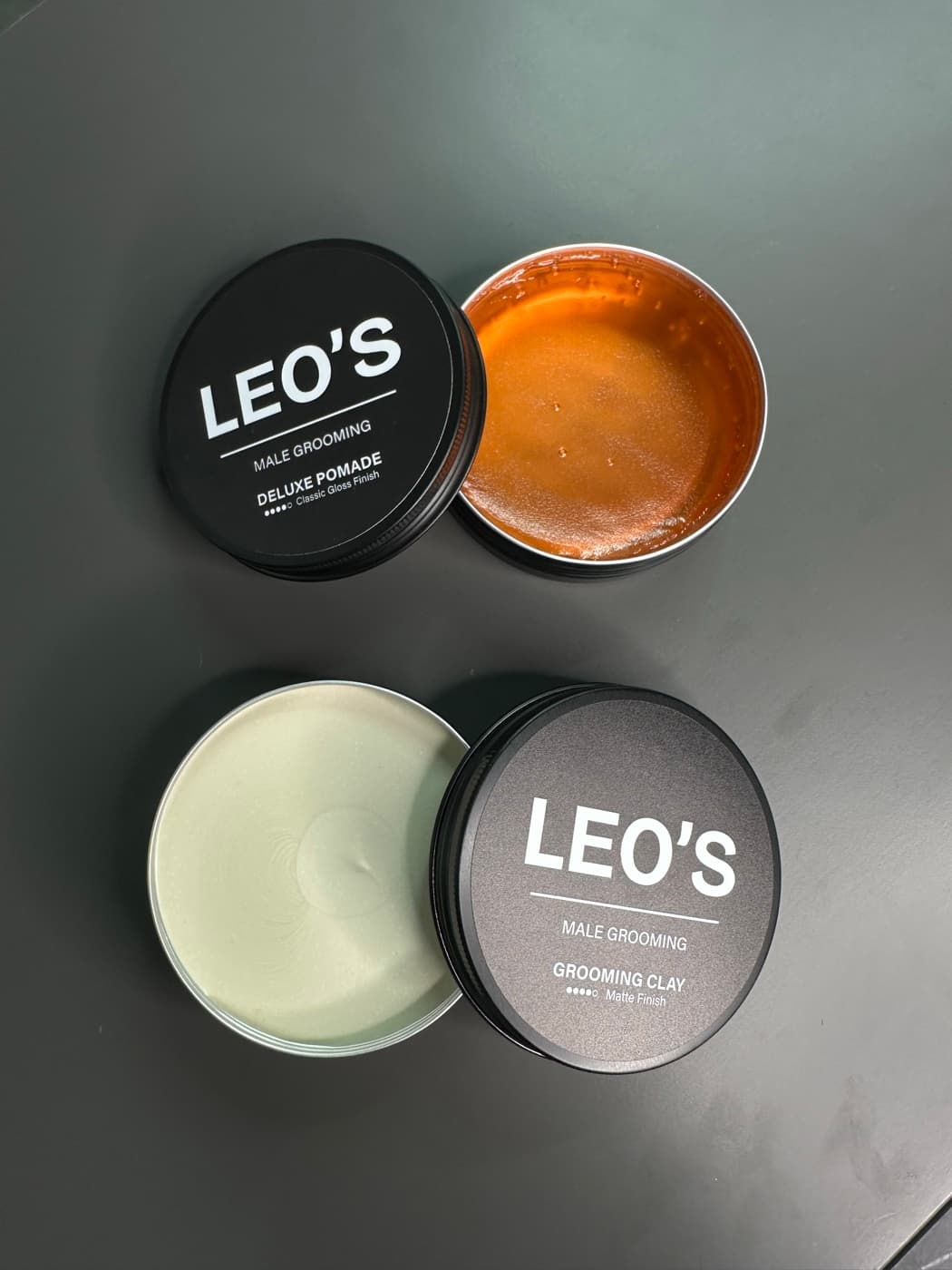 Two open LEO'S tins, Deluxe Pomade in amber and Grooming Clay in pale matte