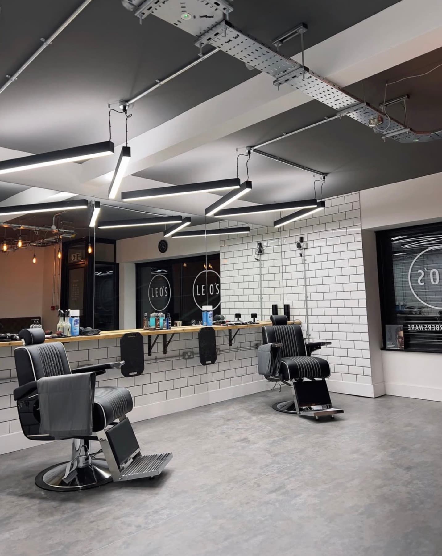 Leo's Barbers seen from the door, showing the barber chairs, the timber shelf along the tiled mirror wall and the LEO'S roundel on the glass
